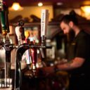 Close-up of a Peller Estates tap at the bar, with a bartender working in the blurred background.