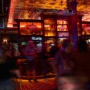 Red-lit bar with pressed-tin ceiling and a 'Heart & Crown' sign, blurred patrons gathered around the bar.