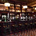 Well-lit bar with Jameson and Bushmills signage, empty stools, and a checkered black-and-white floor.
