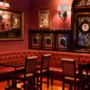 Empty dining nook with red tufted booth seating, stained glass windows, and Heart & Crown branded mirrors on the wall.