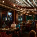 Nighttime patio with a corrugated roof and string lights, guests seated at tables enjoying drinks.