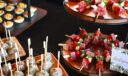 Tiered catering display with deviled eggs, glazed meatballs on skewers, and an antipasto skewer wreath of salami, mozzarella, tomato, and basil.