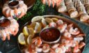 Shrimp cocktail platters with lemon wedges and cocktail sauce, served alongside sliced pinwheel wraps on a catering table.