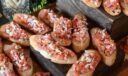 Rows of bruschetta on toasted baguette slices, topped with diced tomato, red onion, and shaved cheese.