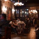 Busy Irish pub dining room with guests enjoying food and drinks at wooden tables beneath warm lighting and stone walls.