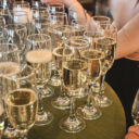 Server pouring champagne into a row of filled champagne flutes on a tray.